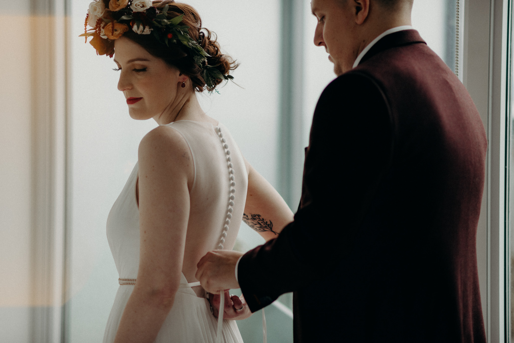 groom buttoning up back of brides dress