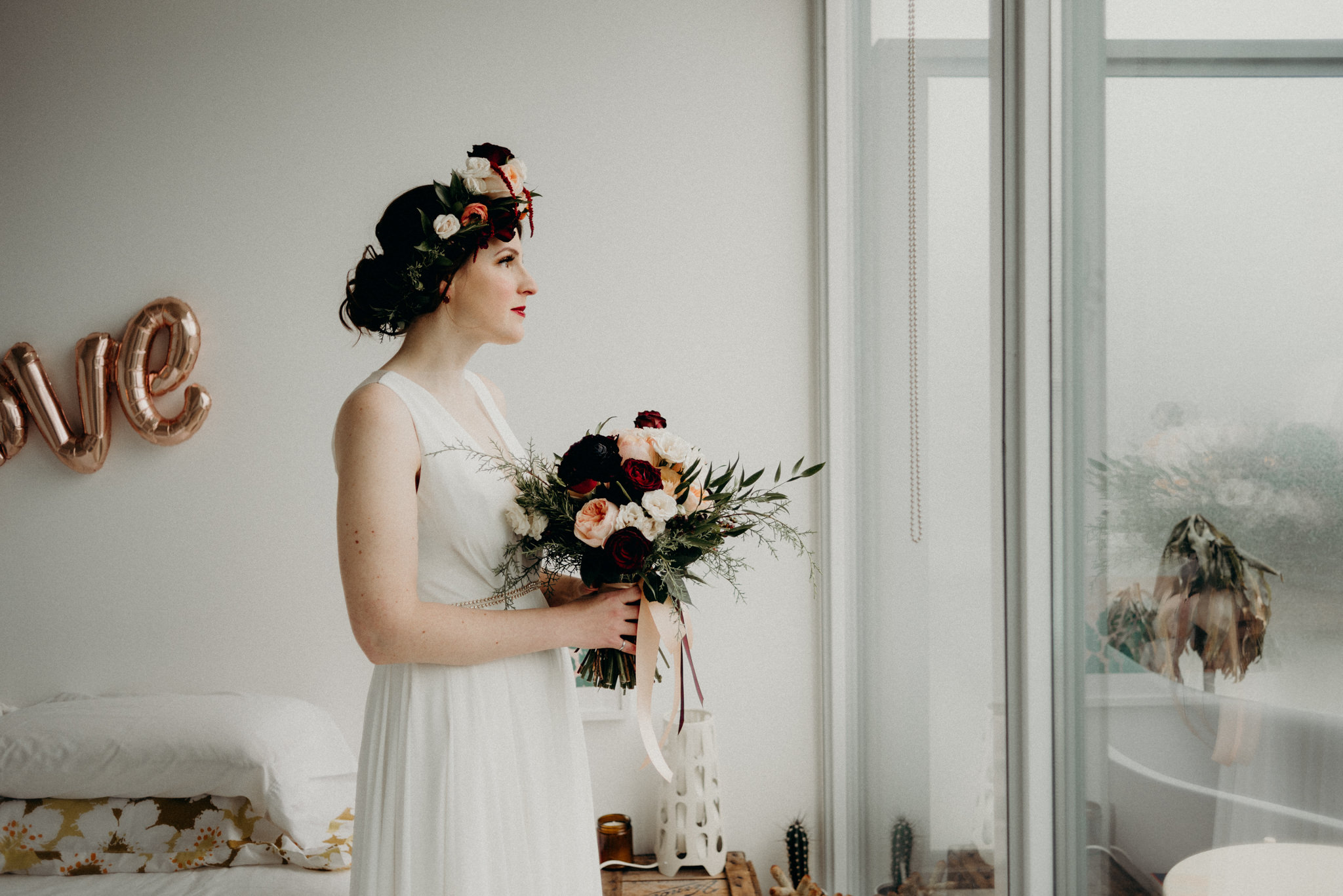 groom buttoning up back of brides dress in bedroom