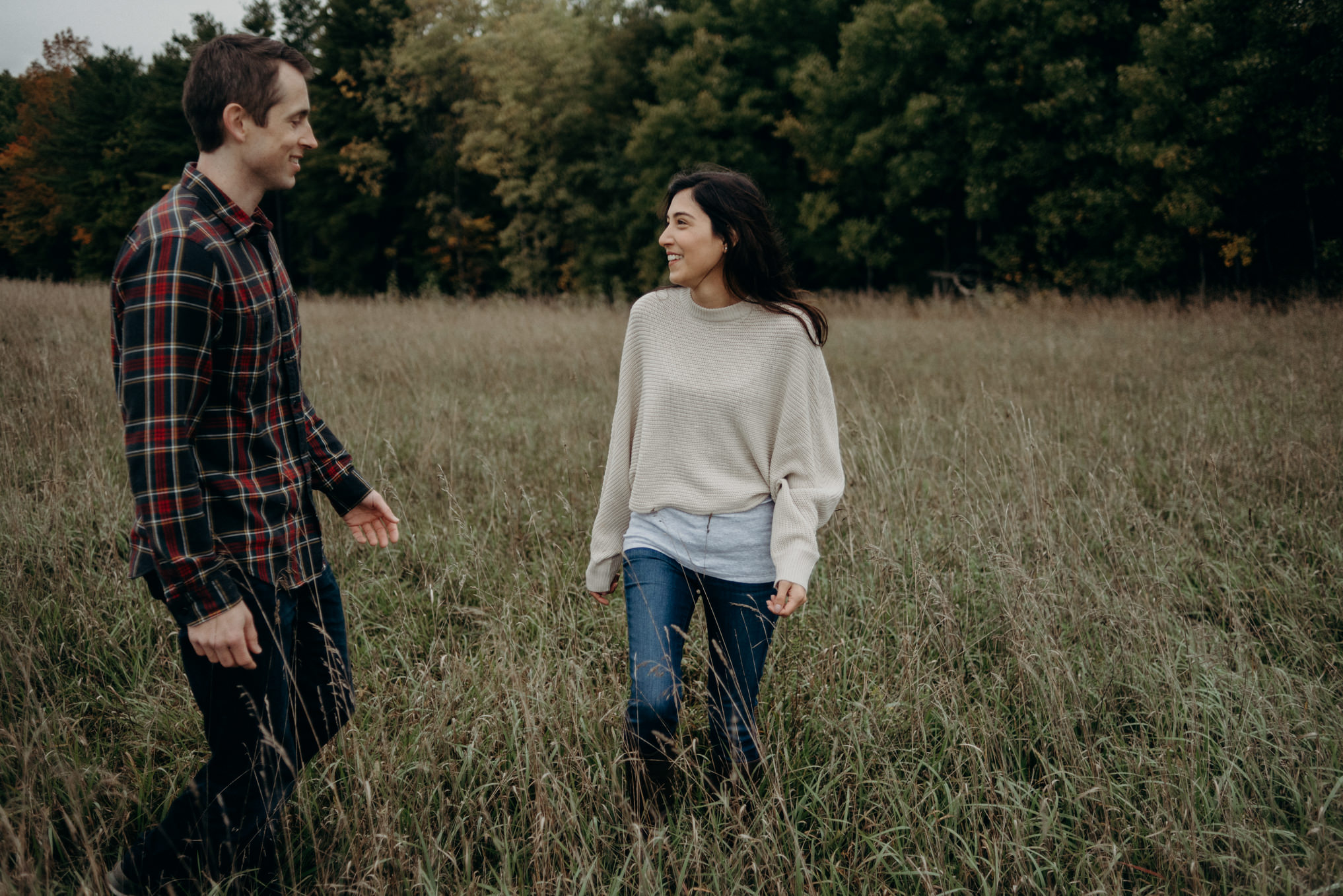 Couple hugging in a field with forest behind them. Whispering Springs couple shoot