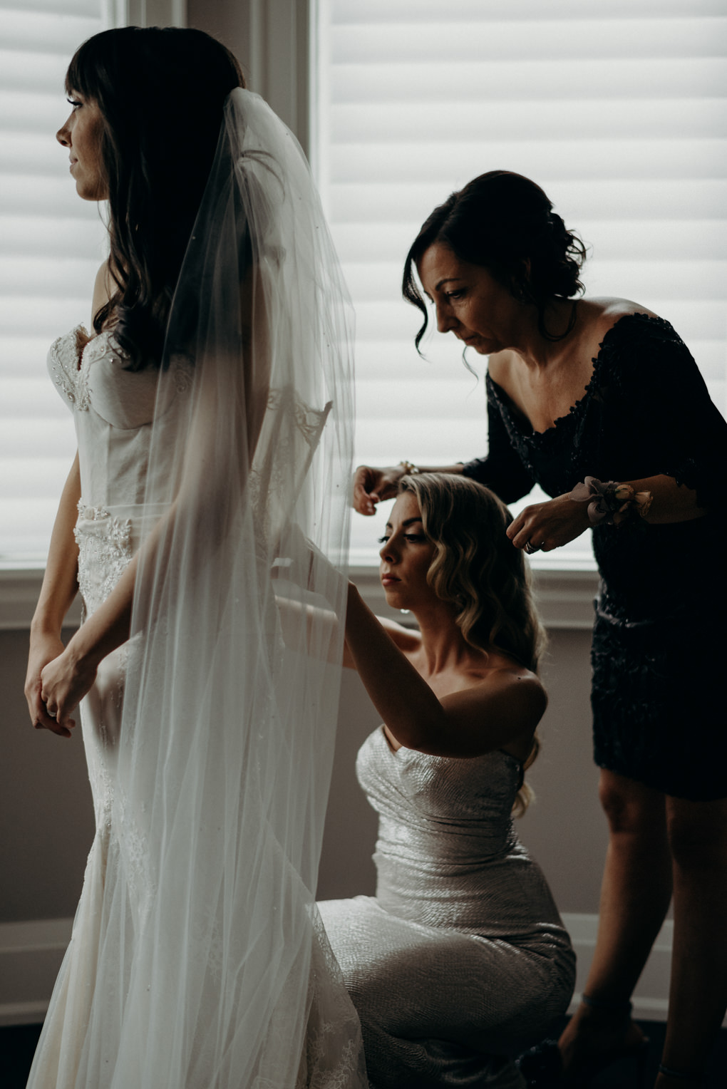 sister and mother of bride helping do up back of dress