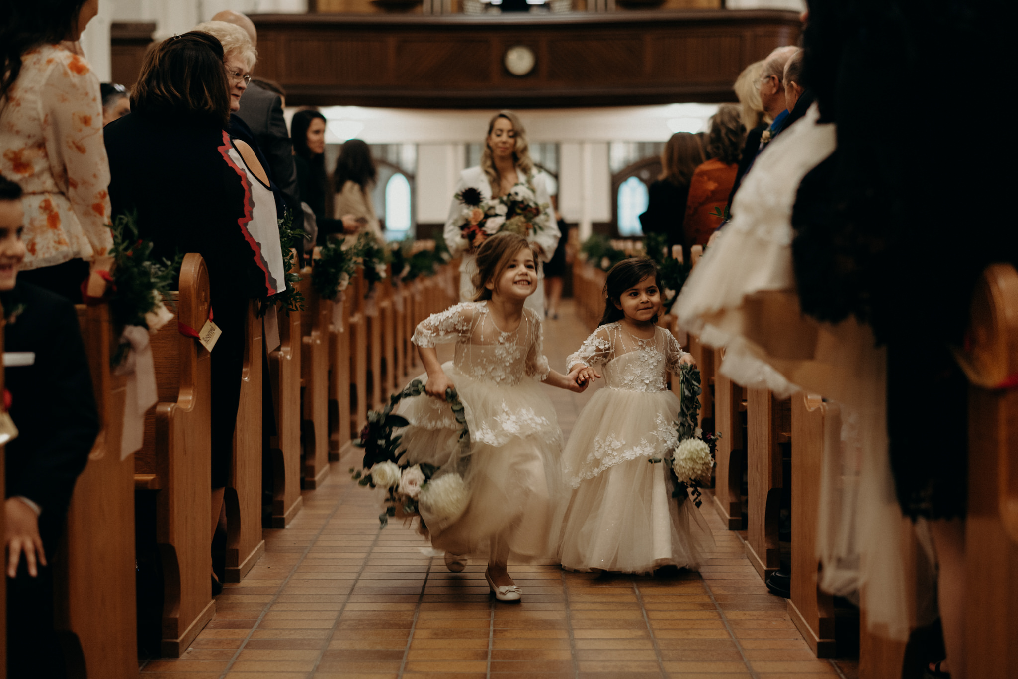 flower girls holding hands and running down aisle of church