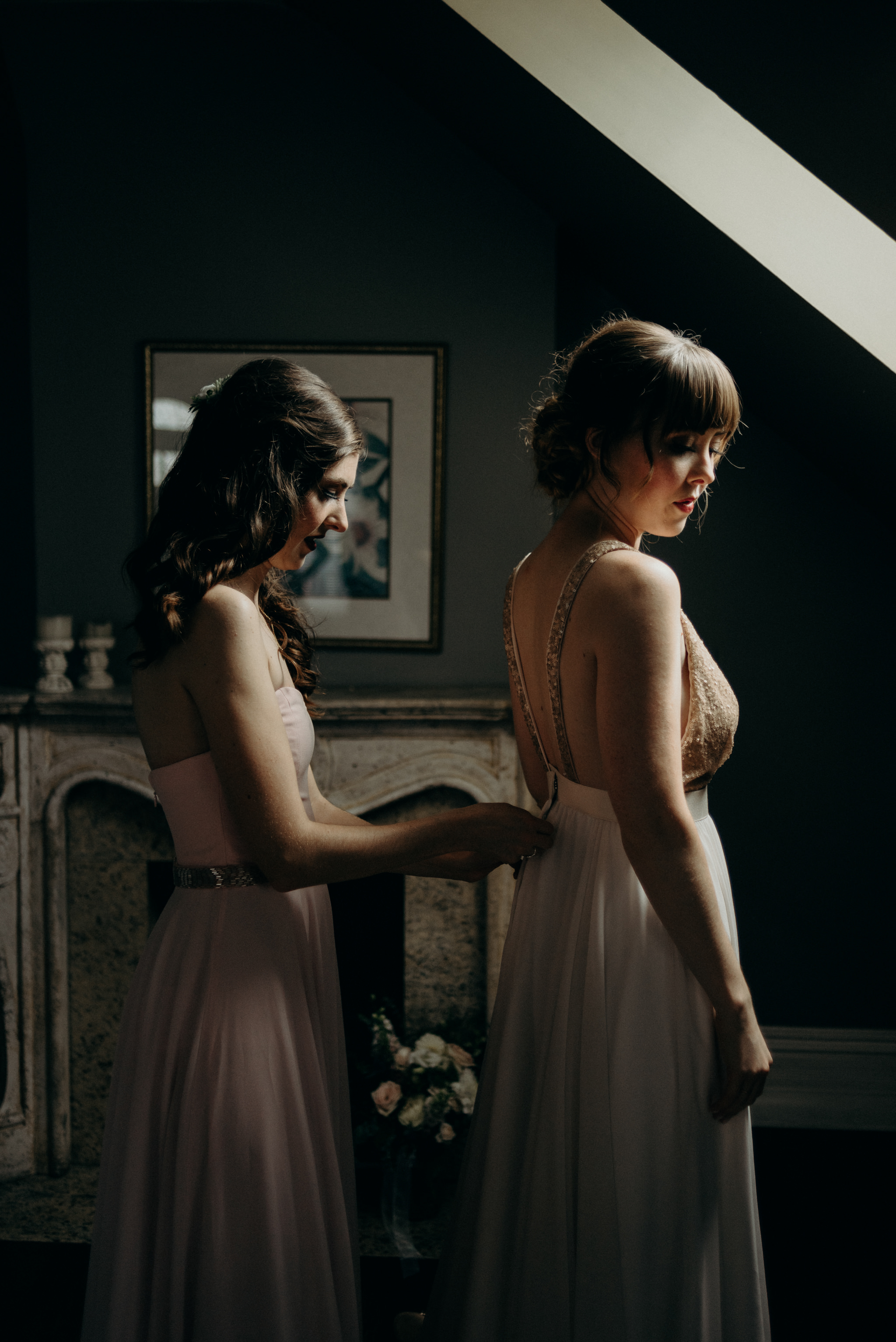 bridesmaid helping bride into dress in attic room with skylight