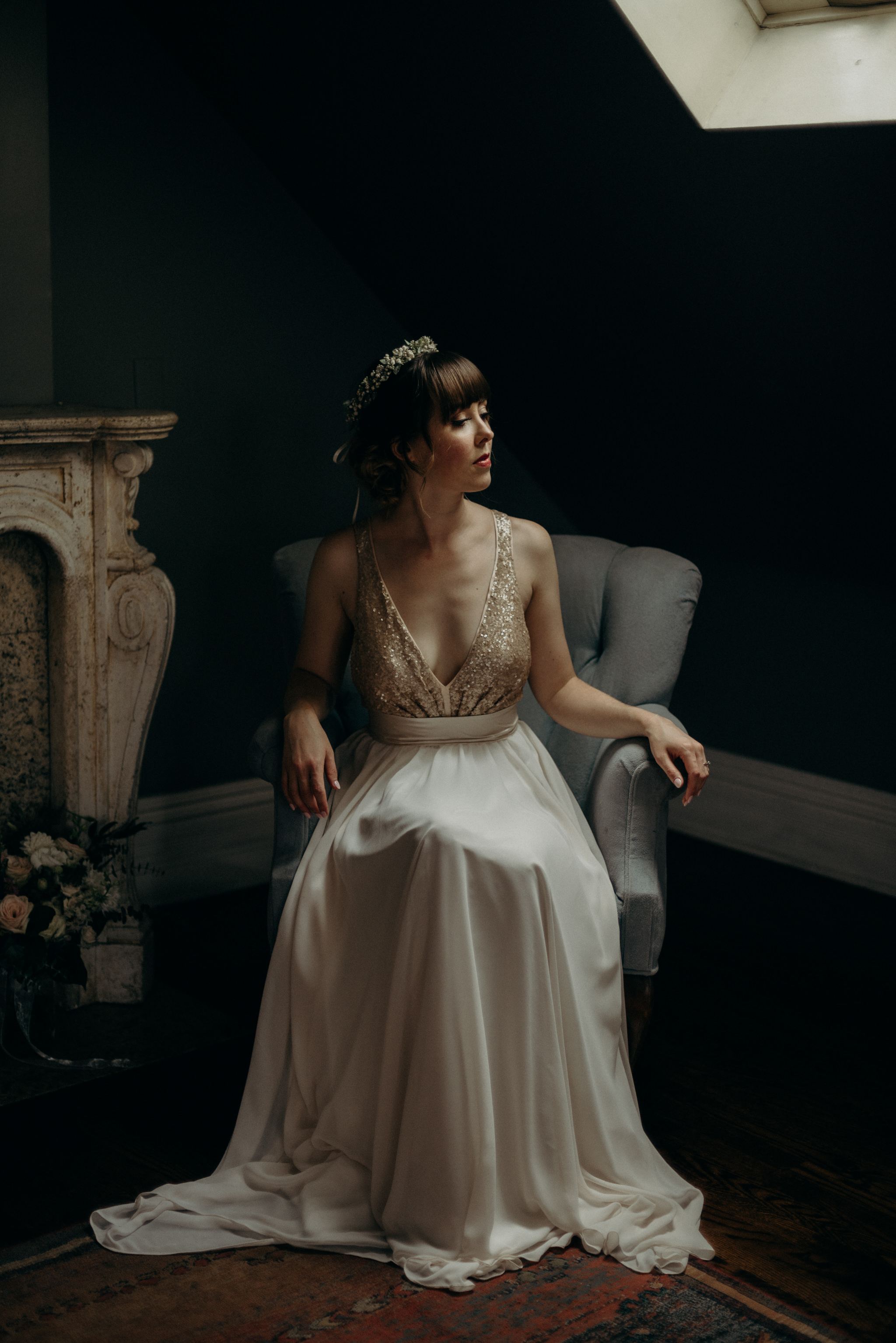 bride sitting in elegant chair in dark room with skylight