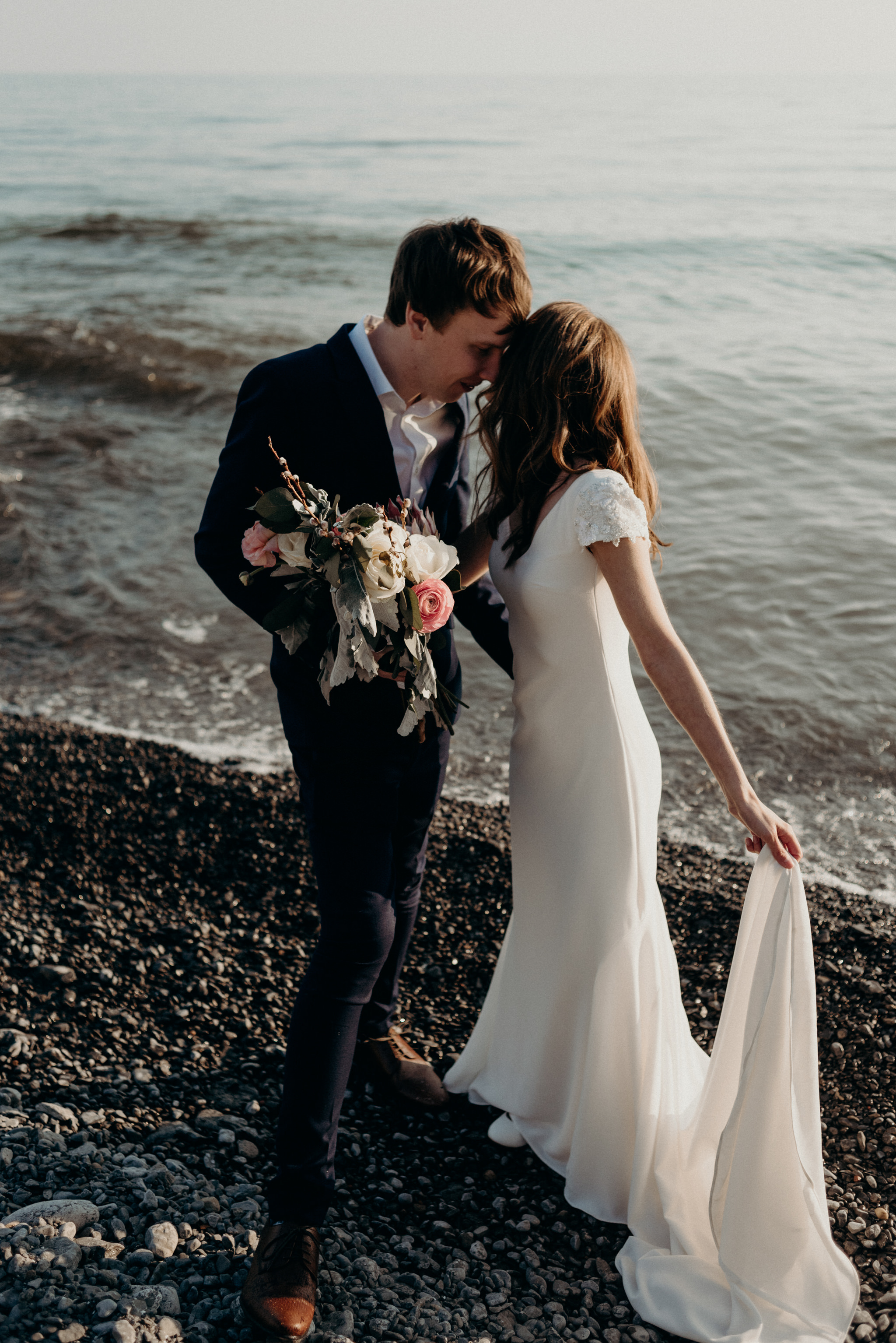 Couple hugging on the beach in front of Drake Devonshire for their elopement