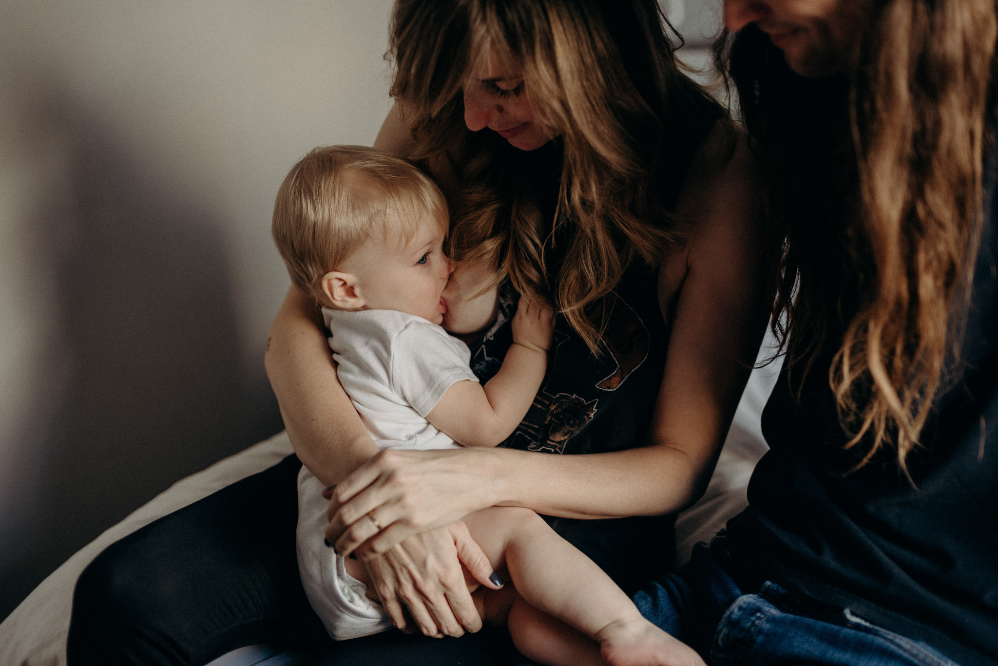 toddler breastfeeding on mom's lap on bed