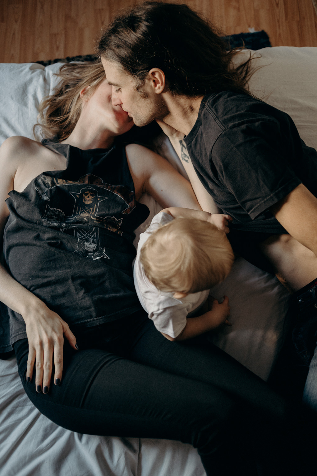 hip young couple lying on bed kissing with toddler between them