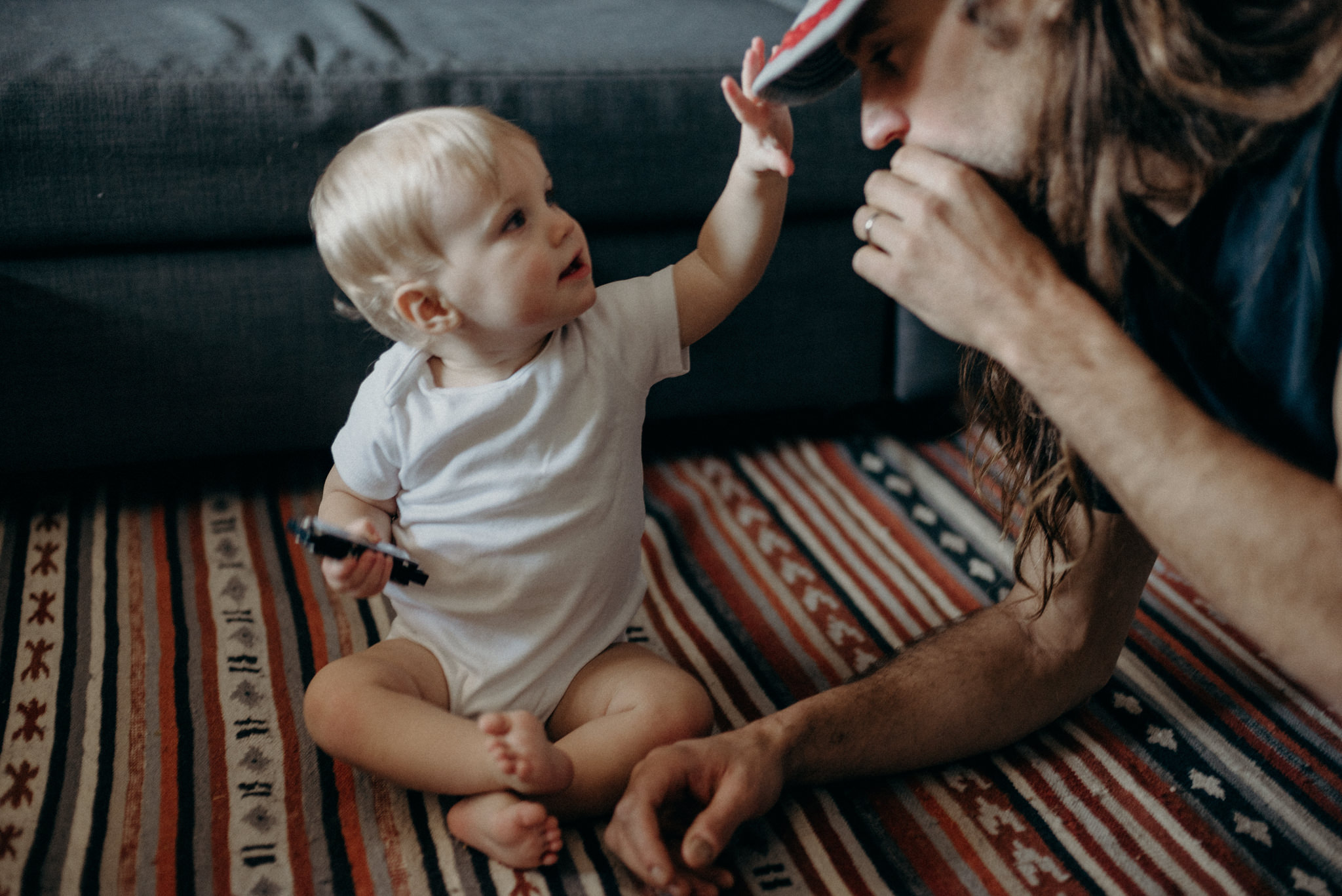 toddler boy playing with dads hat as he plays the harmonica on the carpet