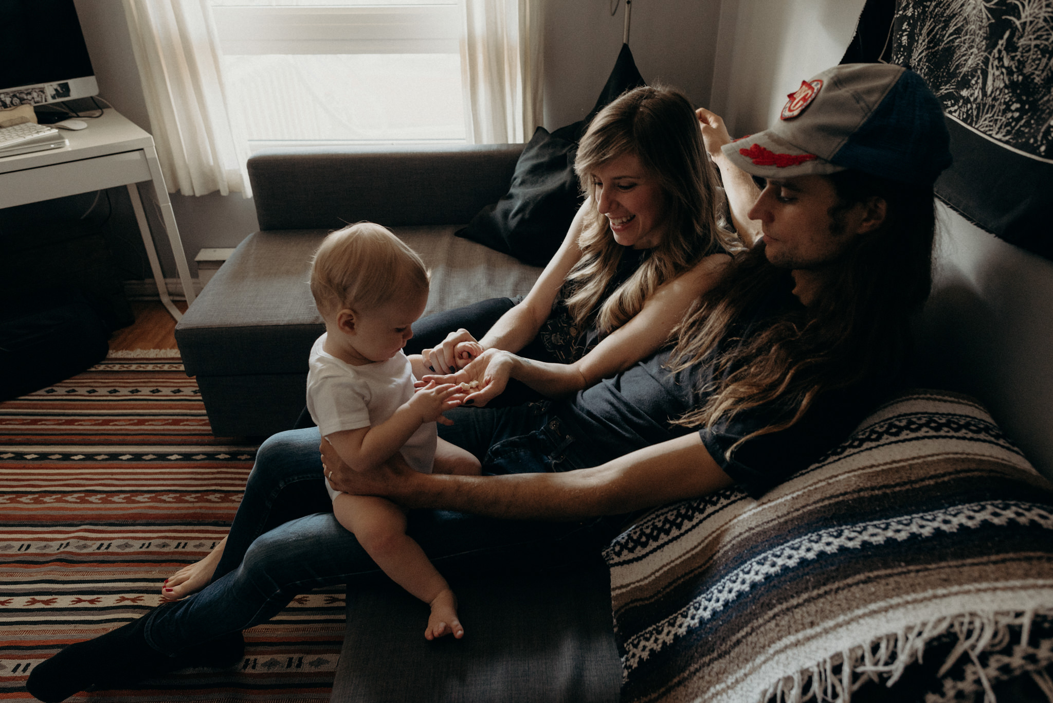 hip young couple sitting on couch in apartment with toddler