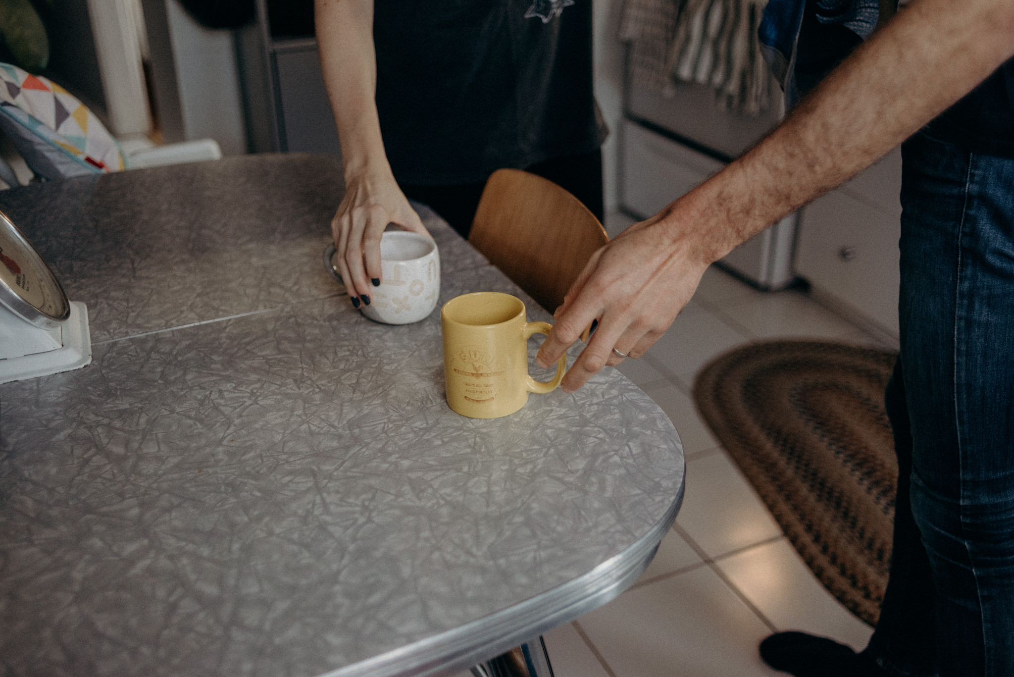 couple reaching for coffee mugs on table in kitchen