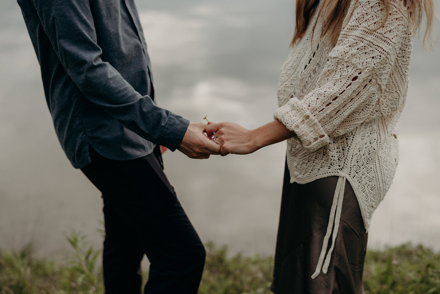 couple holding hands by lake holding flower