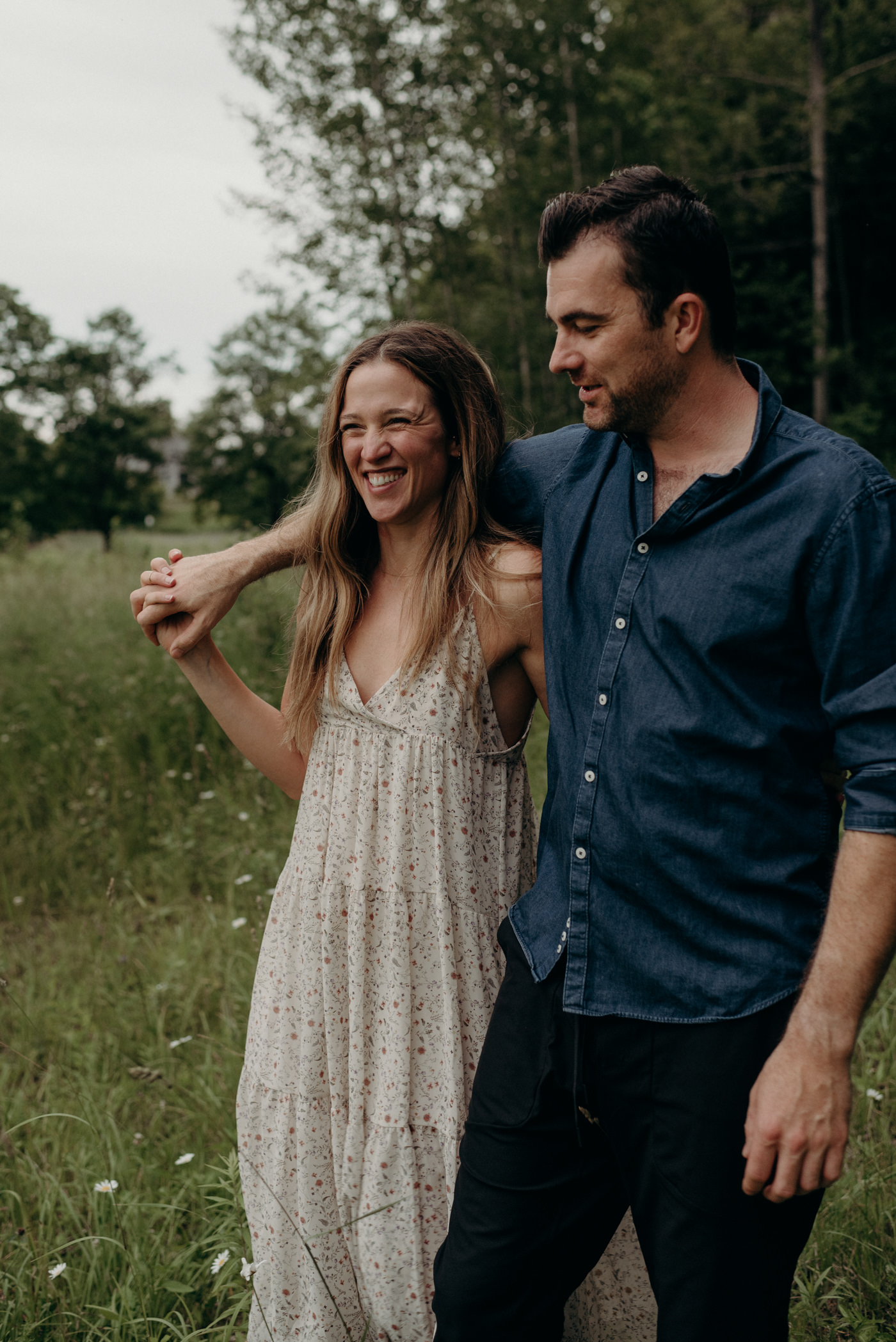 happy couple walking in field of tall grass and flowers for engagement shoot in Stouffville