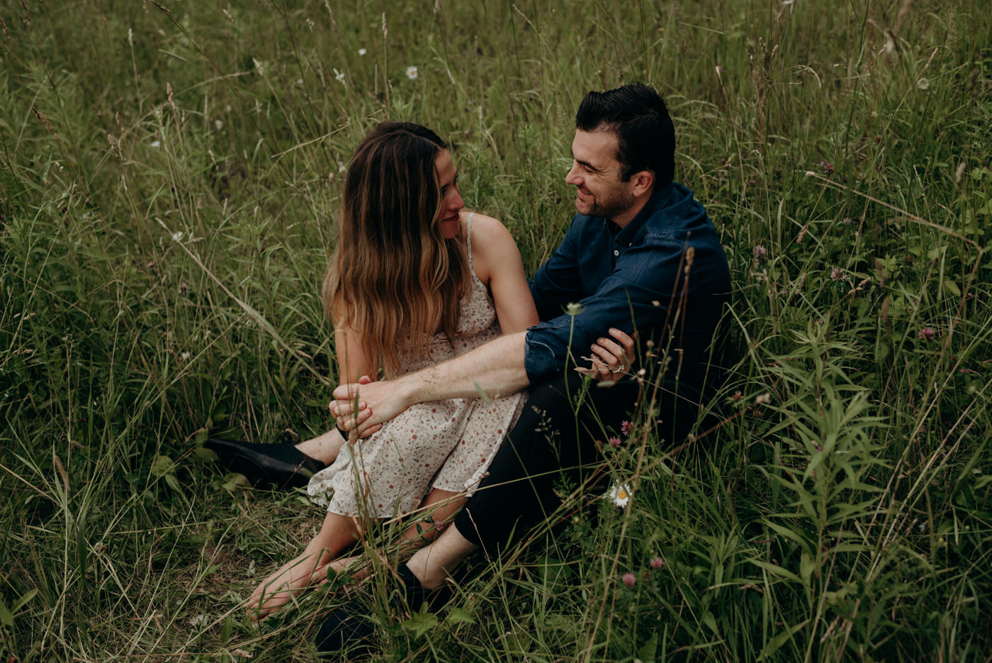 couple sitting in tall grass and looking at each other and smiling