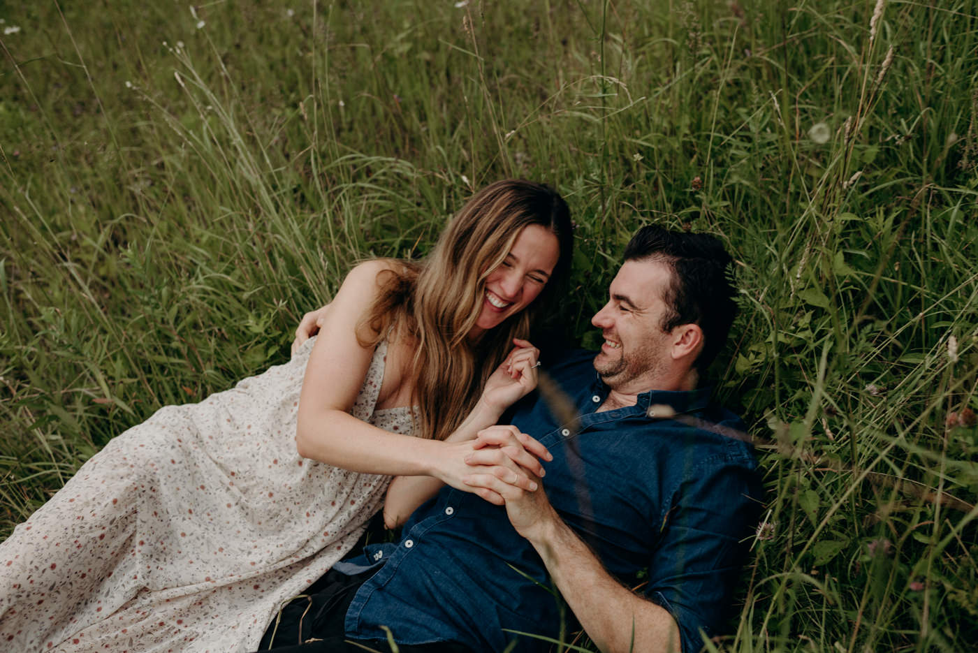 couple laughing and holding hands as they roll in tall grass