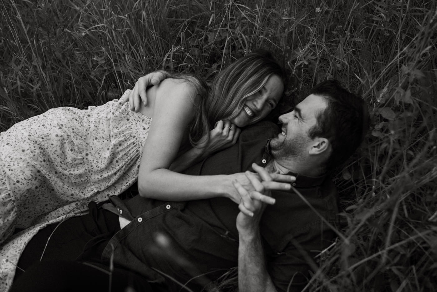 couple laughing and holding hands as they roll in tall grass