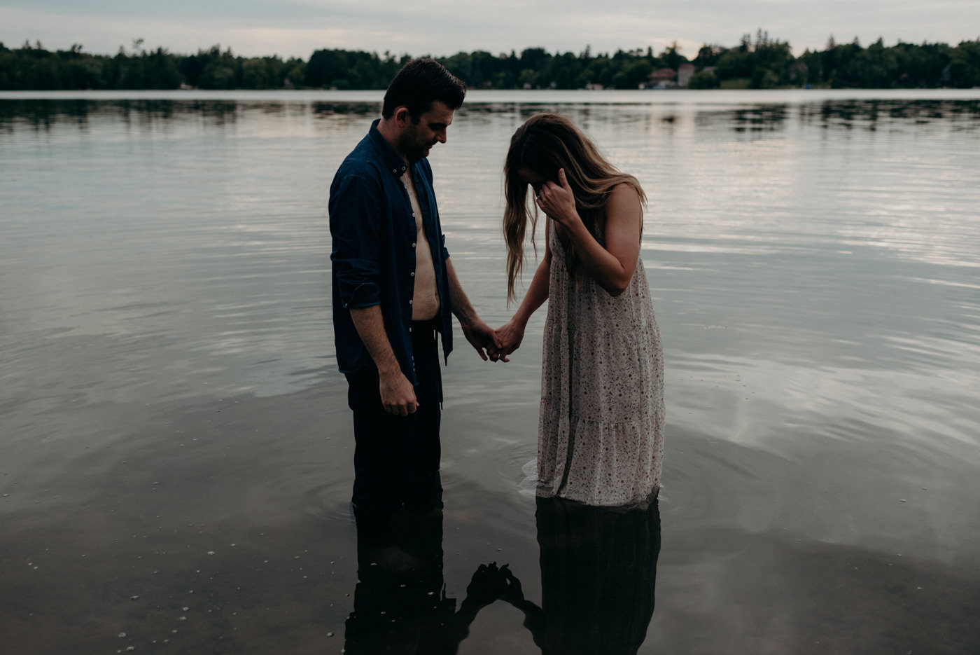 couple holding hands and standing in water at lake