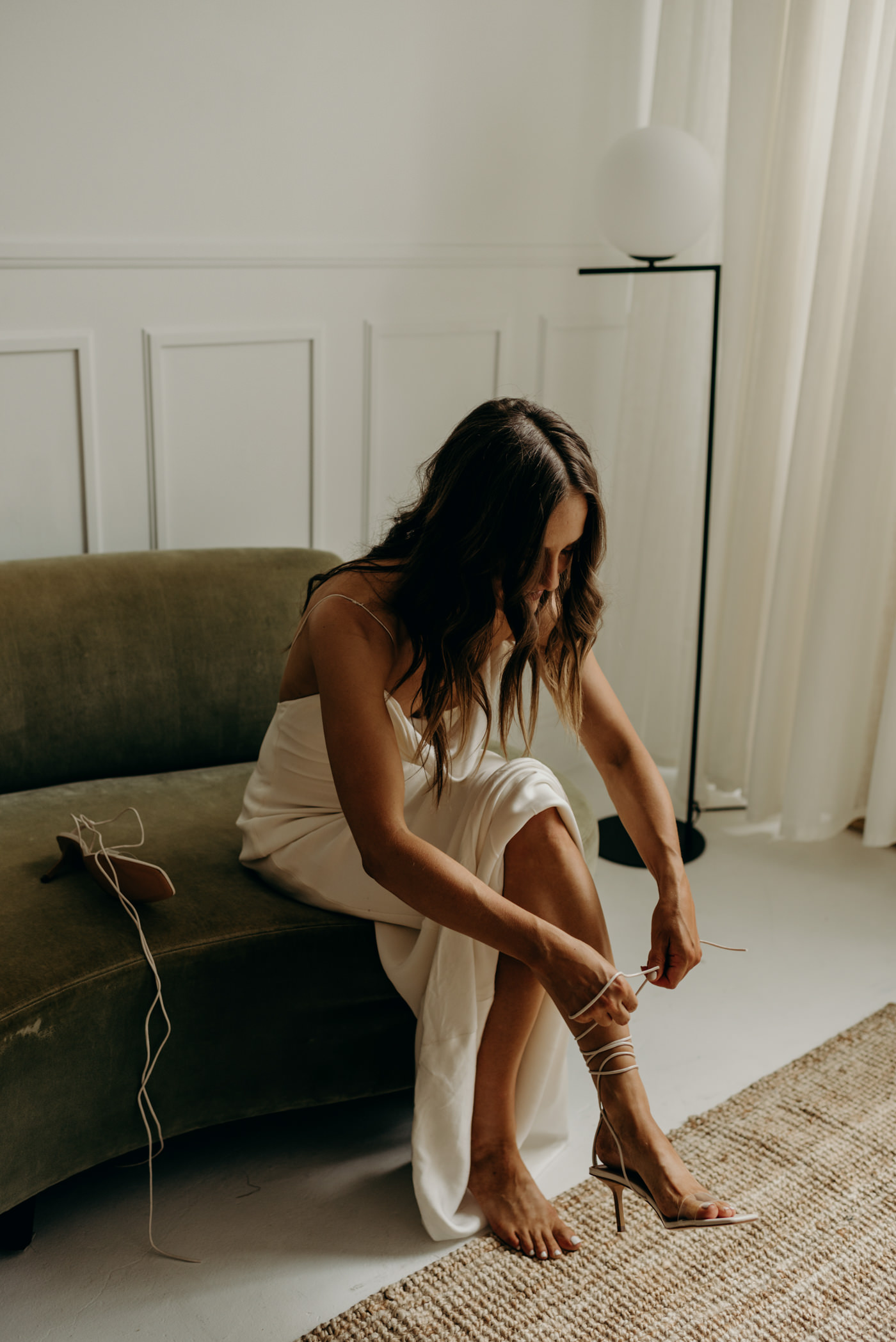 bride tying up shoes while sitting on velvet couch in cool midcentury loft elopement