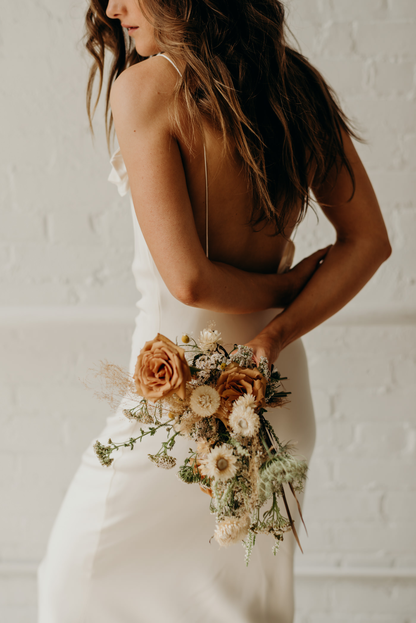 Bride in white brick wall loft wearing Savannah Miller bridal and orange dried flower bouquet