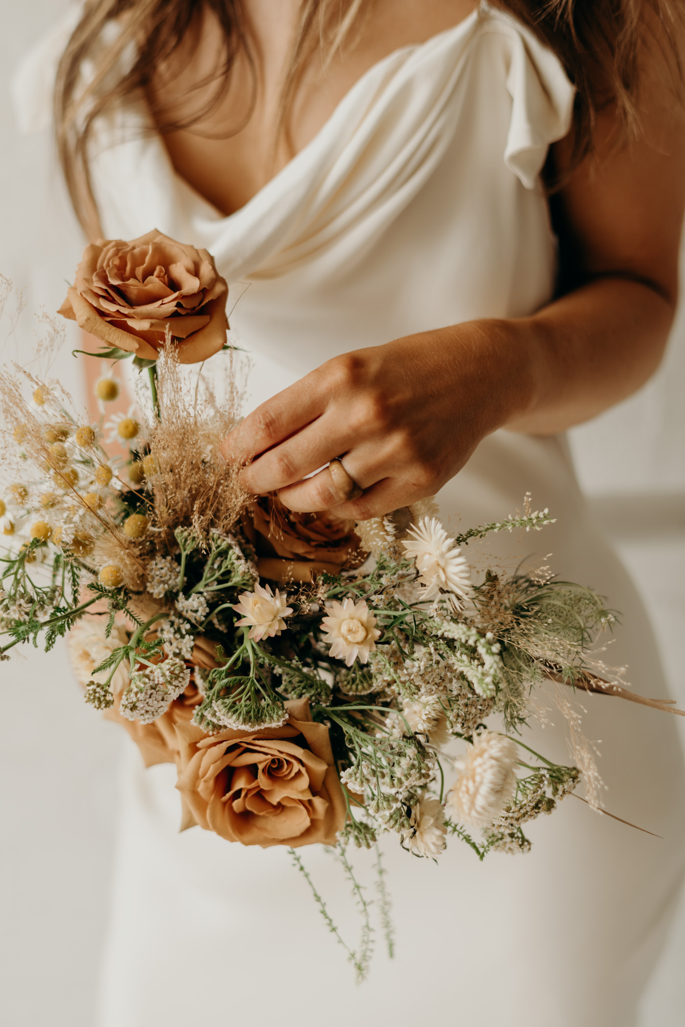 Bride in white brick wall loft wearing Savannah Miller bridal and orange dried flower bouquet