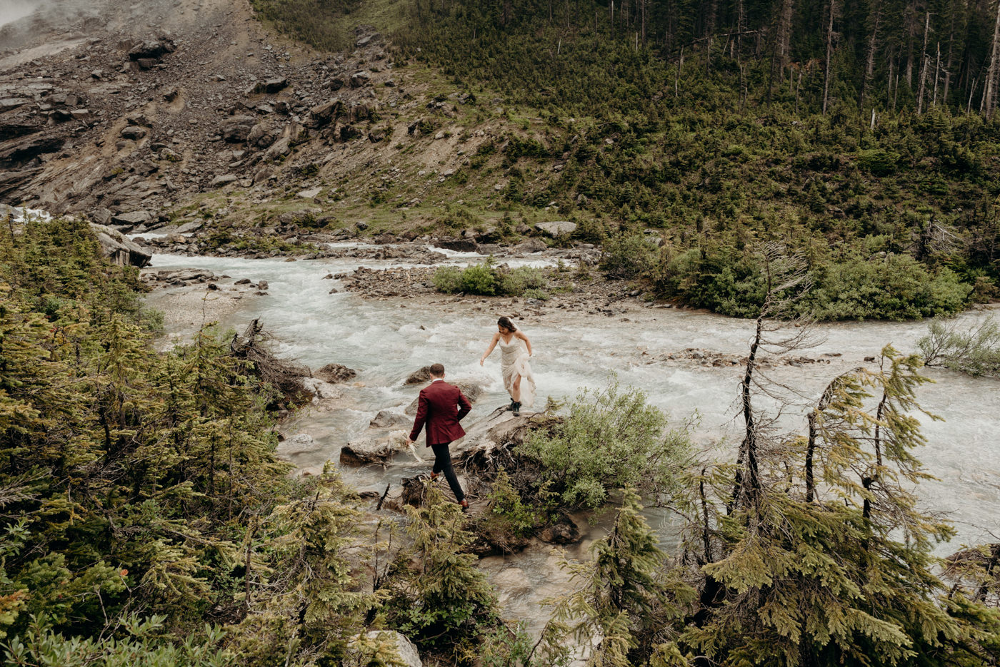 bride and groom hiking to rock in river on their wedding day