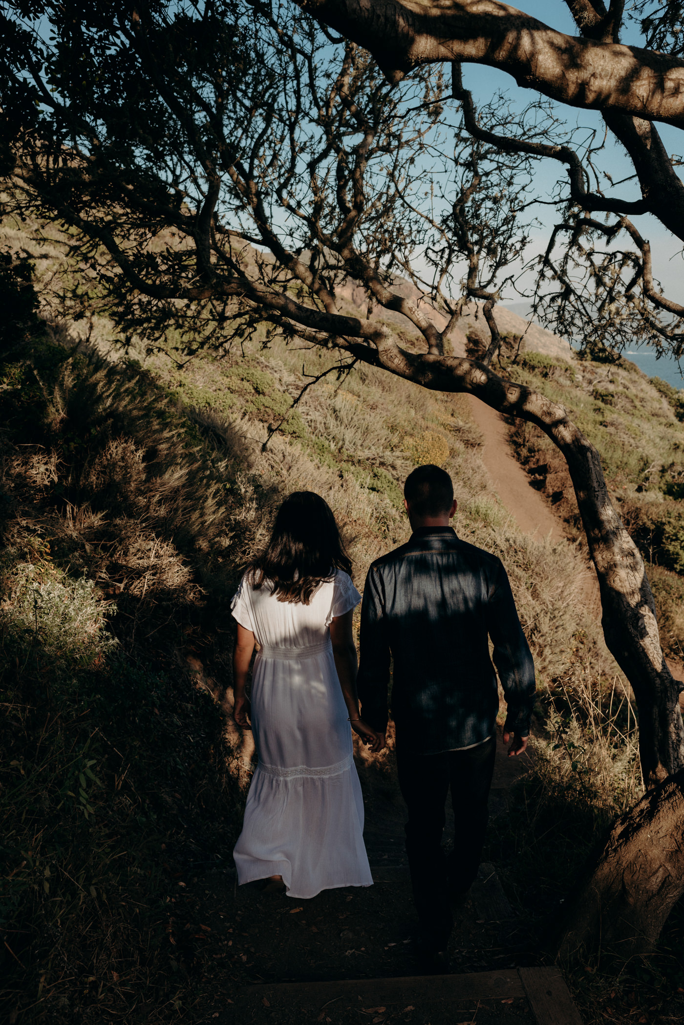 Couple holding hands and walking on trail towards beach at Marin Headlands