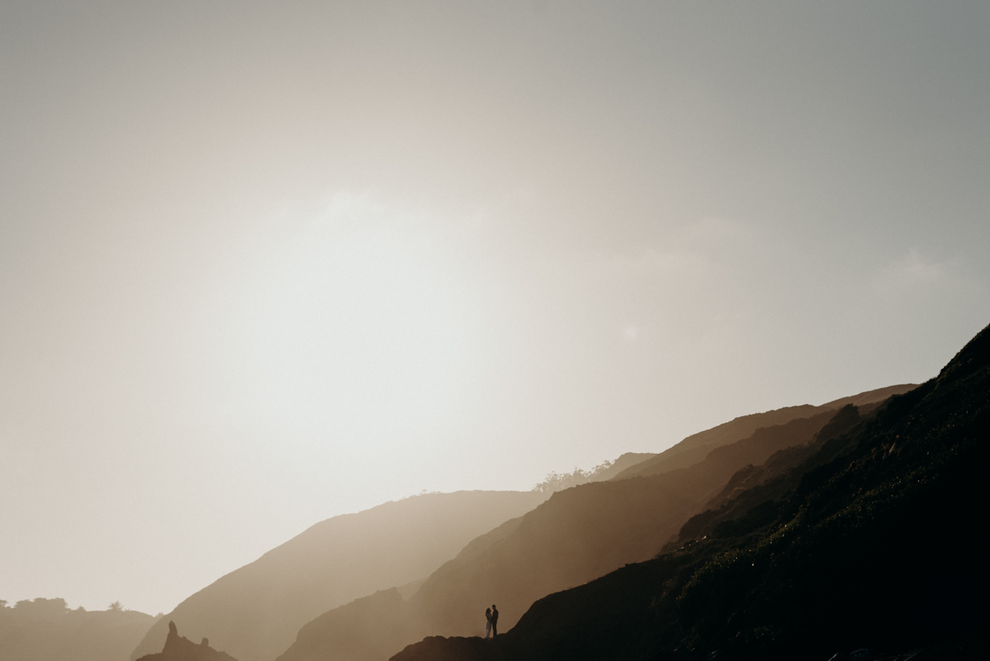 Couple standing on rock in the distance at sunset at Marin Headlands