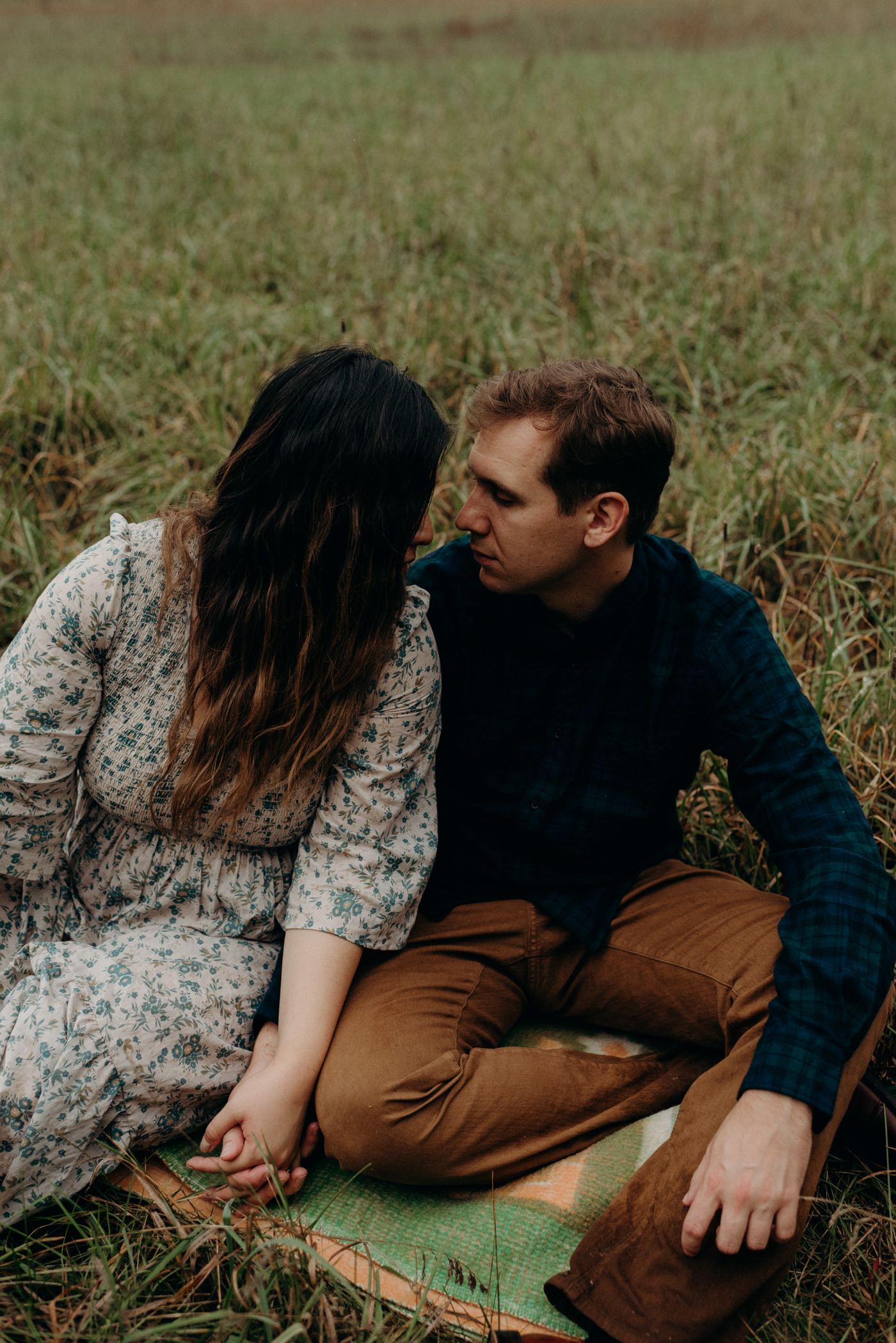 couple holding hands while sitting on blanket on grass