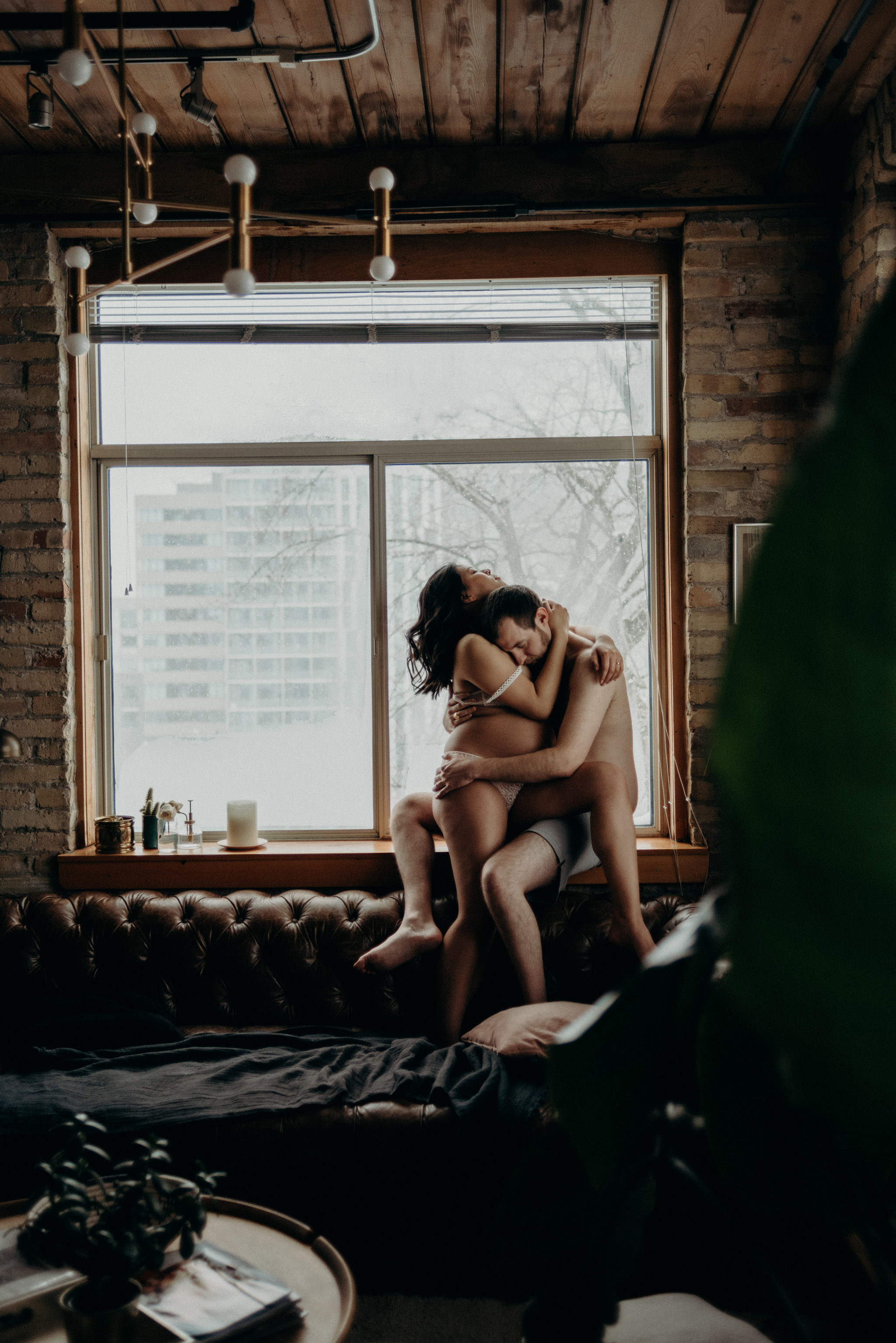 couple sitting on couch of a trendy loft for their indoor Toronto maternity shoot