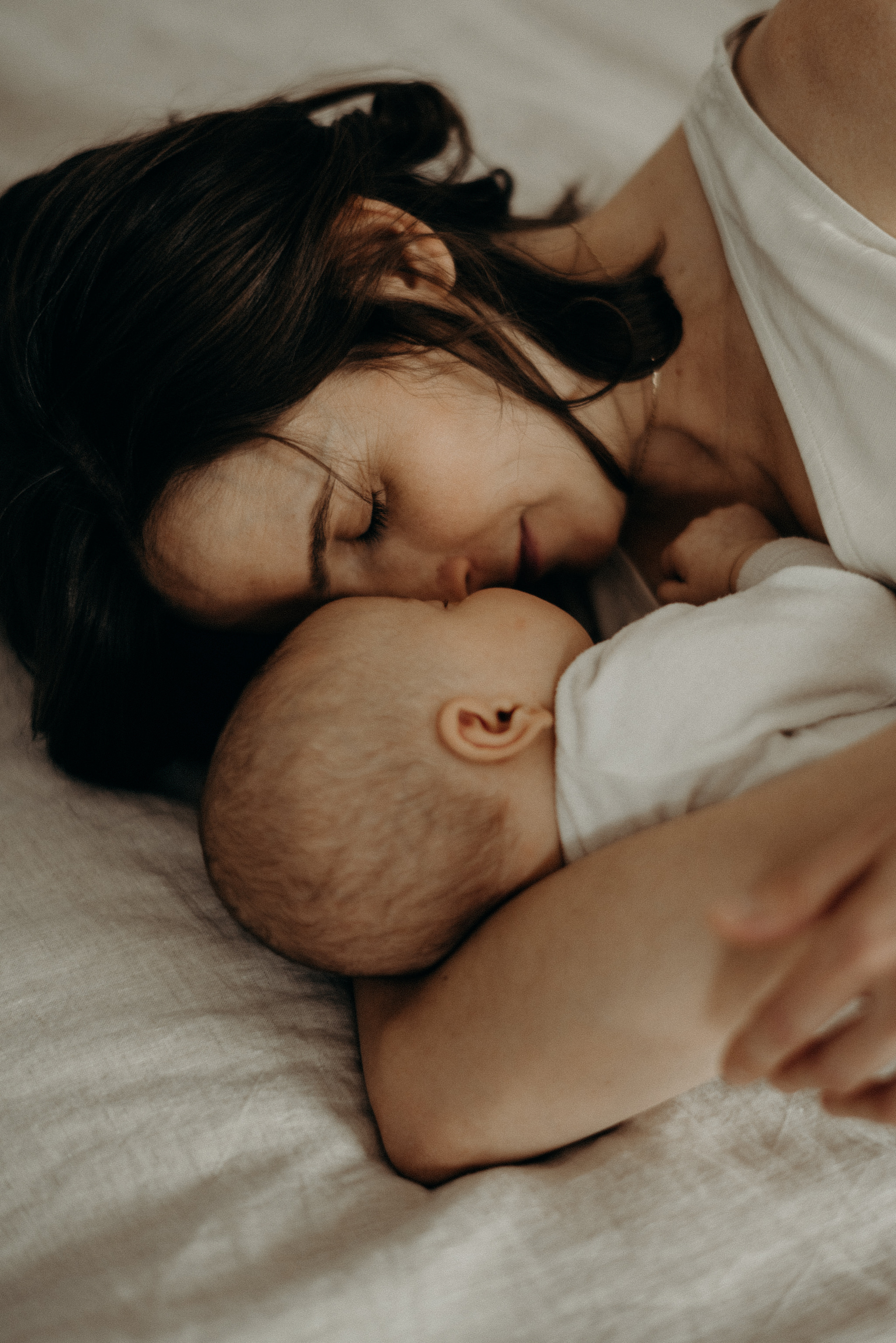 mother cuddling newborn baby in bed