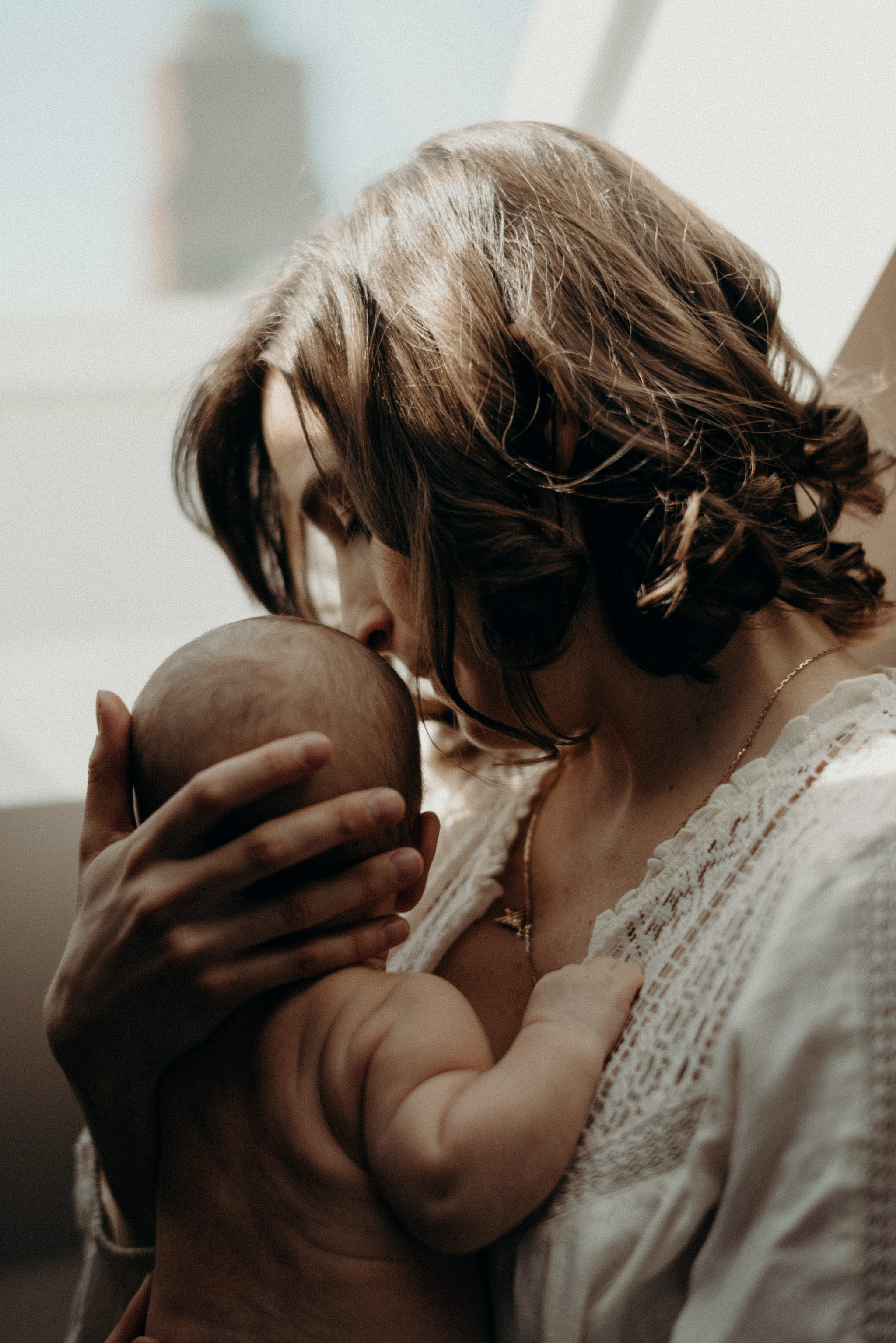 mother holding infant son in the sunlight of their home