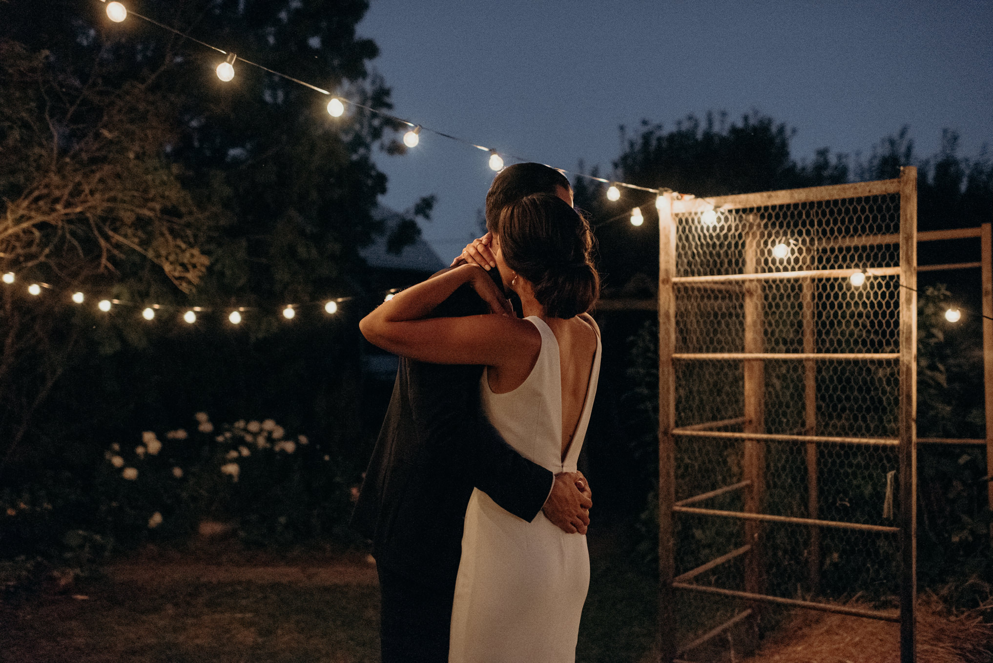 Bride and groom dancing under string lights outside