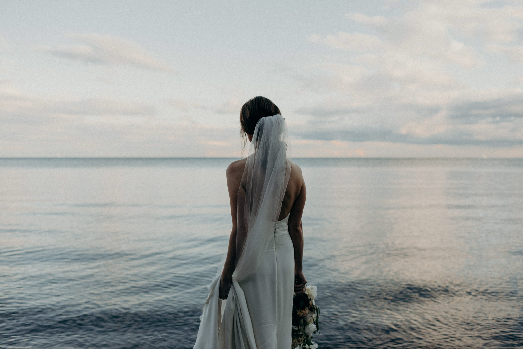 bride looking out onto calm lake Ontario at sunset in Toronto