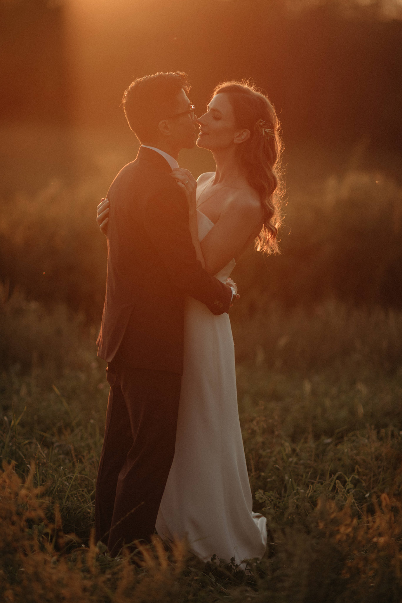 couple standing in field with sunflare sunset light on them as they kiss