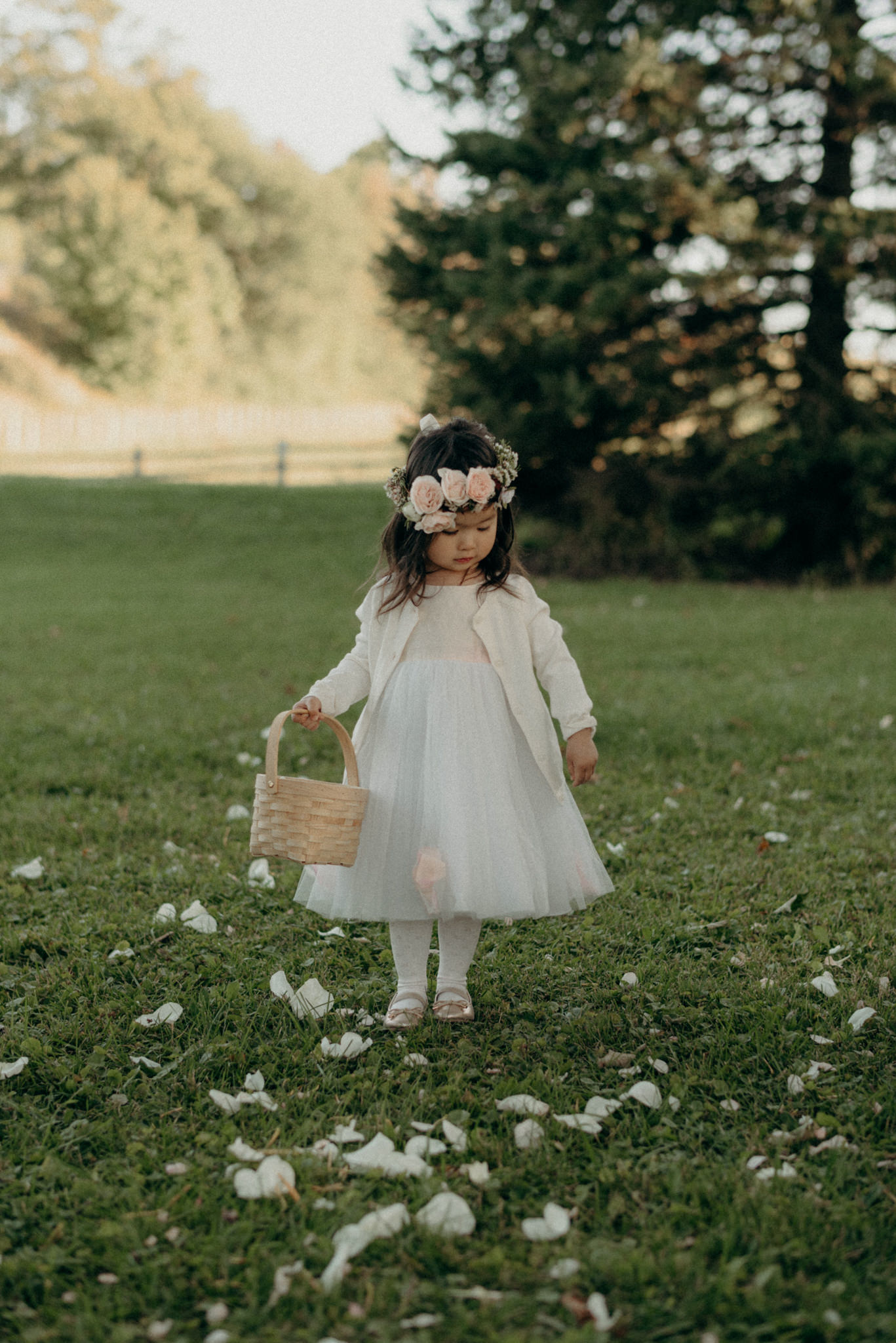 flower girl in floral crown throwing rose pedals down grass aisle