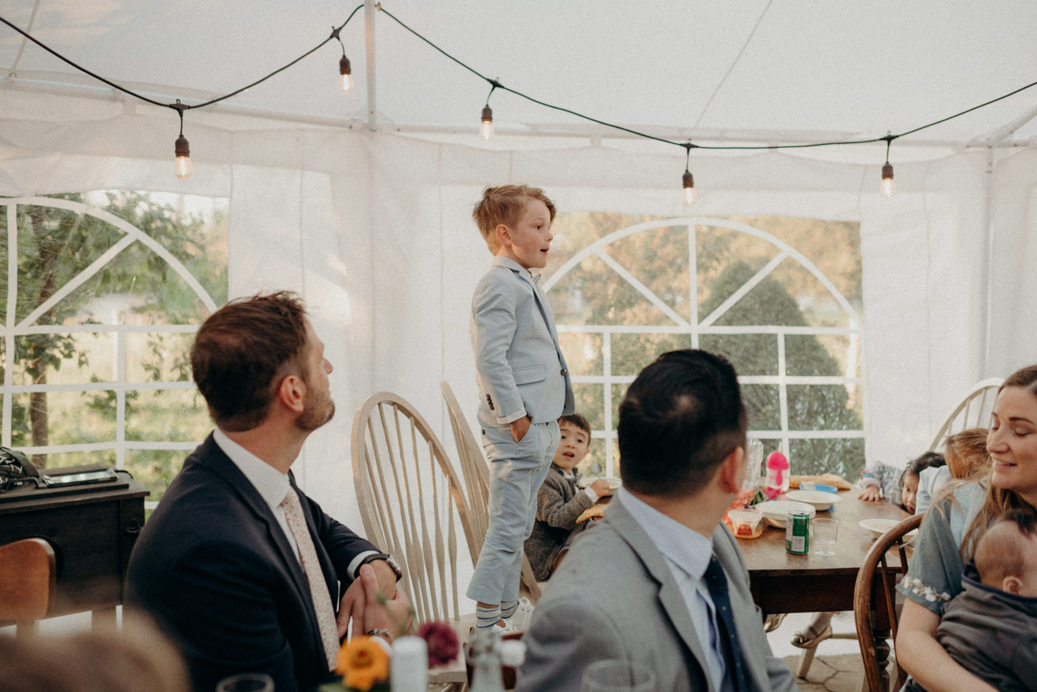 little boy standing on chair saying irish blessing before dinner. intimate tent wedding reception at Good Family Farms